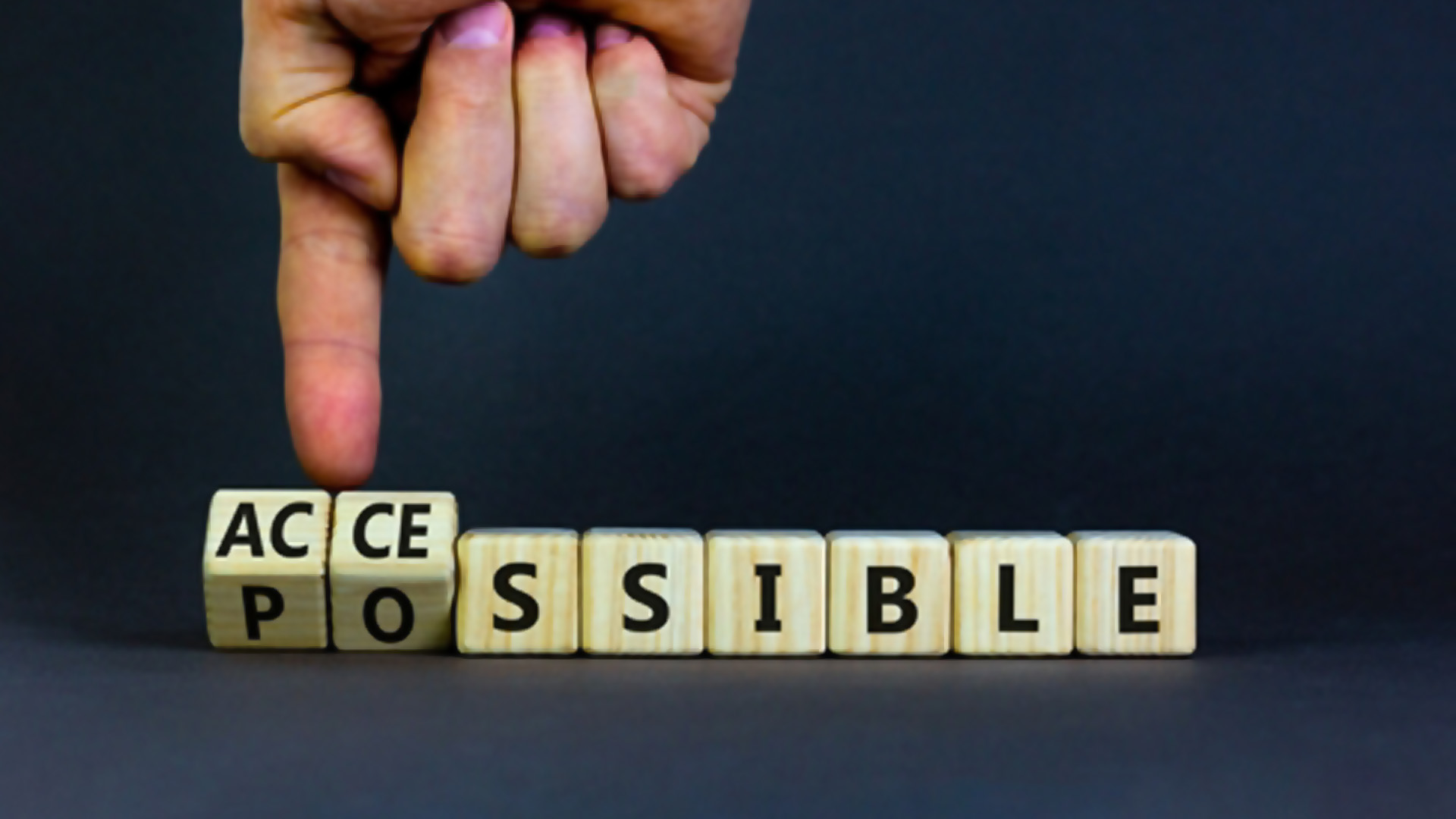 A person’s hand turns wooden cubes and changes the word, possible to accessible.