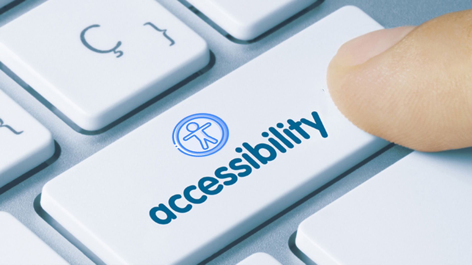 A close-up shows a person’s hand over a key titled, accessibility, on a keyboard. The key has a logo that represents a man with arms extended to the sides.