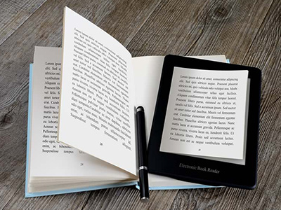 An electronic book reader and a pen placed over an open book on a table.